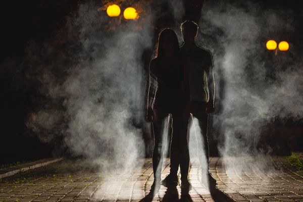 Çift, arka plandaki karanlık sokakta duruyor. Gece vakti.