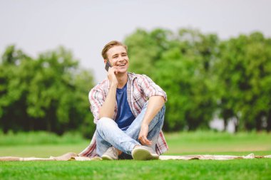 Yakışıklı adam yere oturup telefon ediyor.