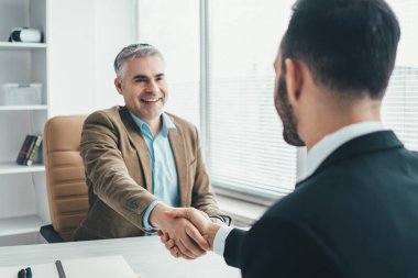 Ofis masasının üstünde el sıkışan iki işadamı.