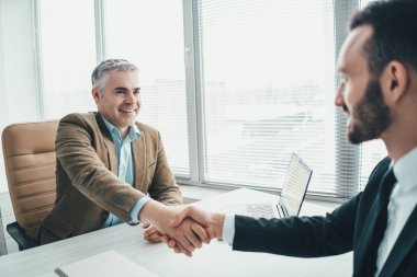 Ofis masasının üstünde el sıkışan mutlu iş adamları.