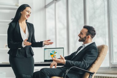 Ofis masasının yanında konuşan mutlu adam ve bir kadın.