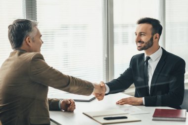 Ofisteki bardağın üzerinden el sıkışan iki mutlu iş adamı.