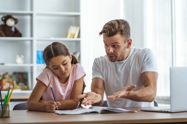 Kızgın baba ve kızı masada ödev yapıyor.
