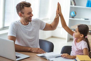 Baba ve kızı masada oturmuş el kol hareketi yapıyorlar.