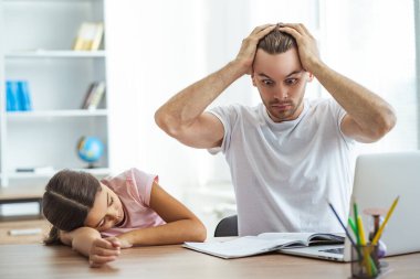 Yorgun baba ve kızı masada ödev yapıyor.