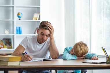 Uykulu adam ve masada ödev yapan bir çocuk.