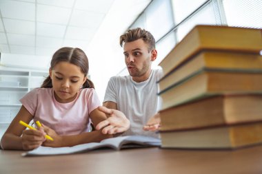 Kızgın adam ve bir kız masada ödev yapıyorlar.