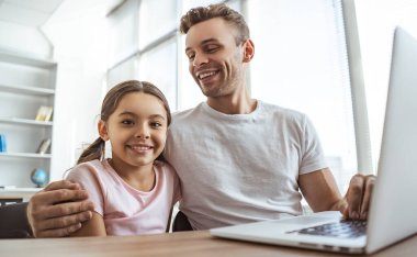 Mutlu baba ve dizüstü bilgisayarı olan kızı masada oturuyorlar.