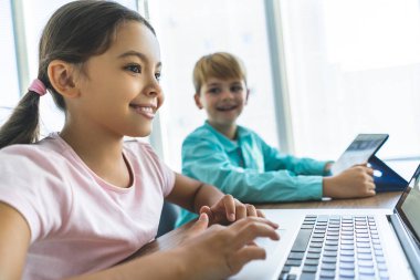 Masada dizüstü bilgisayar ve tabletle oturan mutlu kız ve oğlan.