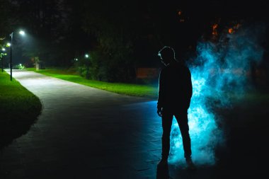 Parkta bir dumanın yanında duran adam. Akşam vakti.