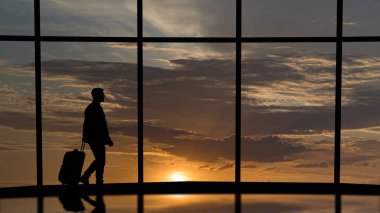 Bavullu adam iş merkezindeki büyük pencerelerin yanında yürüyor.