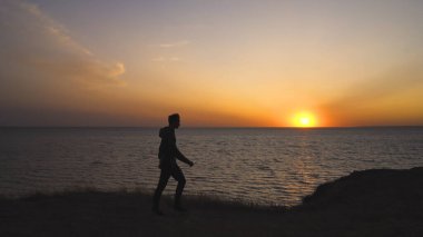 Deniz kenarındaki güzel günbatımı arka planında yürüyen adam.