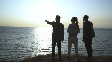 Deniz manzaralı arka planda duran üç genç.