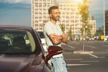 Yakışıklı adam park yerinde yeni arabanın yanında duruyor.