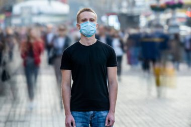 Yüzünde tıbbi maske olan adam şehir sokağının ortasında duruyor.