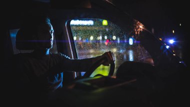 Genç adam yağmurlu bir gecede arabada oturur. 