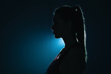 Karanlık odada duran fitness kızı silueti.