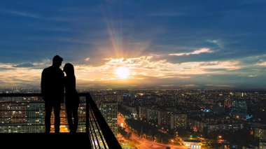 Şehrin arka planında, balkonda duran romantik çift.
