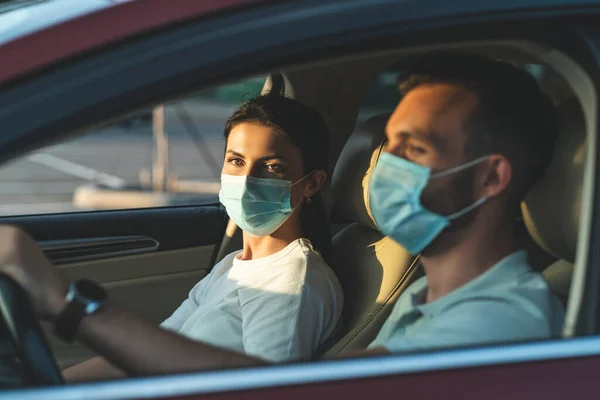 The young couple in masks are sitting in the car