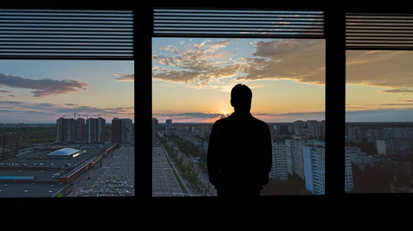 那个孤独的男人站在城市背景下的窗边 — 图库照片