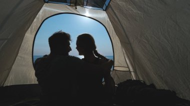 Kamp çadırında güzel deniz kenarına karşı oturan çift.