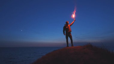 Elinde sopayla dağın tepesinde duran deniz manzaralı adam.