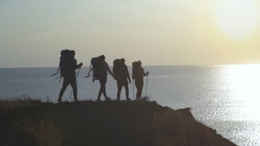 Sırt çantalı turistler deniz kenarındaki dağ manzarasında yürüyorlar.