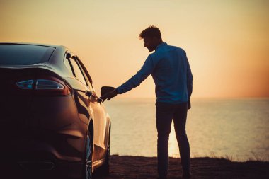 Deniz kıyısında arabanın yanında duran yakışıklı adam.