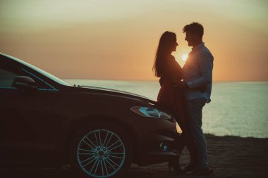Güzel sahil arka planında arabanın yanında duran adam ve kadın.