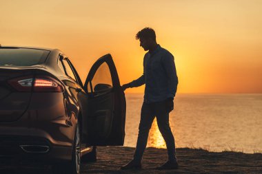 Deniz kıyısında arabanın yanında duran yakışıklı adam.