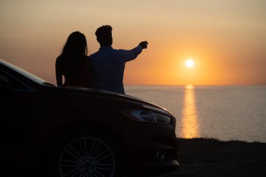 Güzel sahil arka planında arabanın yanında duran adam ve kadın.