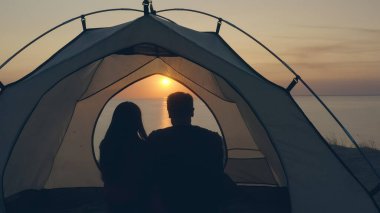 Adam ve kadın deniz kenarındaki kamp çadırında oturuyorlar.