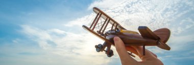 Mavi gökyüzü arka planında tahta bir uçağı olan el.