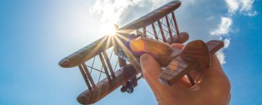 El, bulutun arka planında bir ahşap uçağı tutuyor.