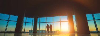 İki adam günbatımı arka planında panoramik pencerenin yanında duruyor.