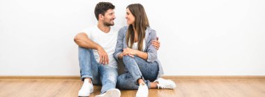 Mutlu çift beyaz duvarın yanında oturuyor.