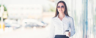 Güneş gözlüklü güzel iş kadını bavuluyla yürüyor.