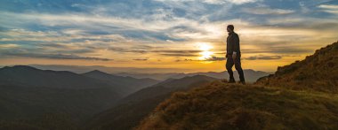 Resimli bir günbatımıyla kayanın üzerinde duran adam.