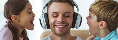 Masada bir kız ve bir çocukla oynayan kulaklıklı mutlu baba.