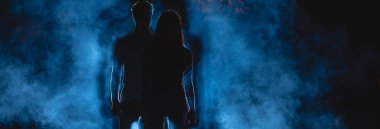 Çift, mavi dumanlı arka planda, karanlık sokakta duruyor. Gece vakti.