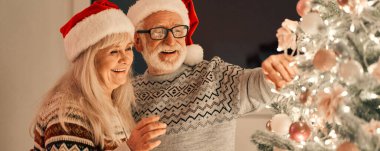 Mutlu yaşlı çift Noel ağacını süslüyor.