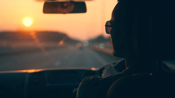 The man driving the auto along the urban highway on the sunset background