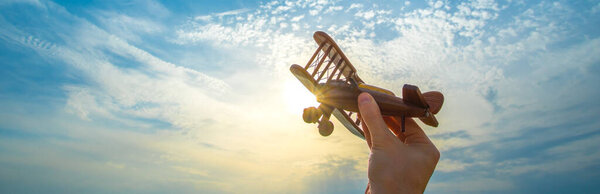 The hand with a wooden airplane on the blue sky background
