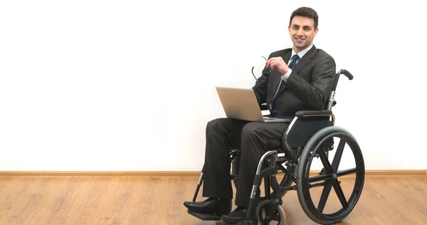 The smile man in a wheelchair sitting with a laptop on a white wall background