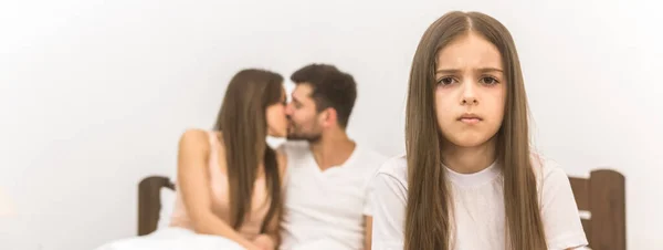 Das Traurige Mädchen Sitzt Auf Dem Hintergrund Der Küssenden Eltern — Stockfoto