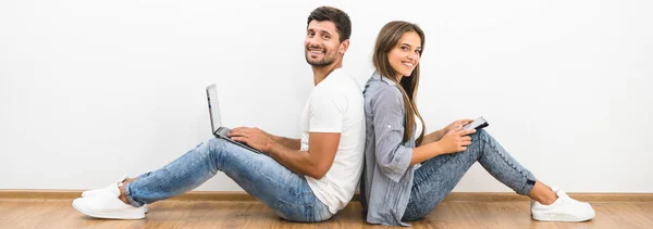 Para Uśmiechnięta Siedzi Laptopem Tabletem Przy Pustej Ścianie — Zdjęcie stockowe
