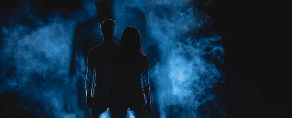 The man and woman stand on a dark alley on the blue fume background. night time