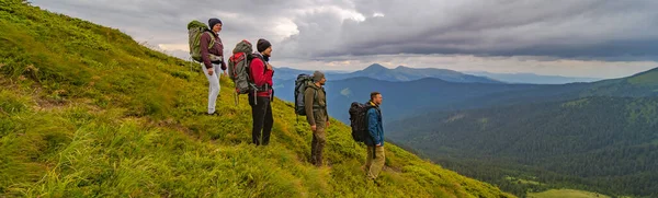 The four active people with backpacks standing on the green mountain