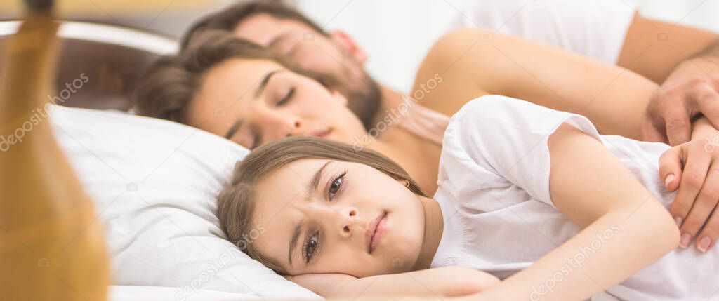 The girl lay near the sleeping parents on the bed