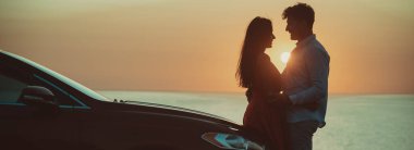 Güzel sahil arka planında arabanın yanında duran adam ve kadın.